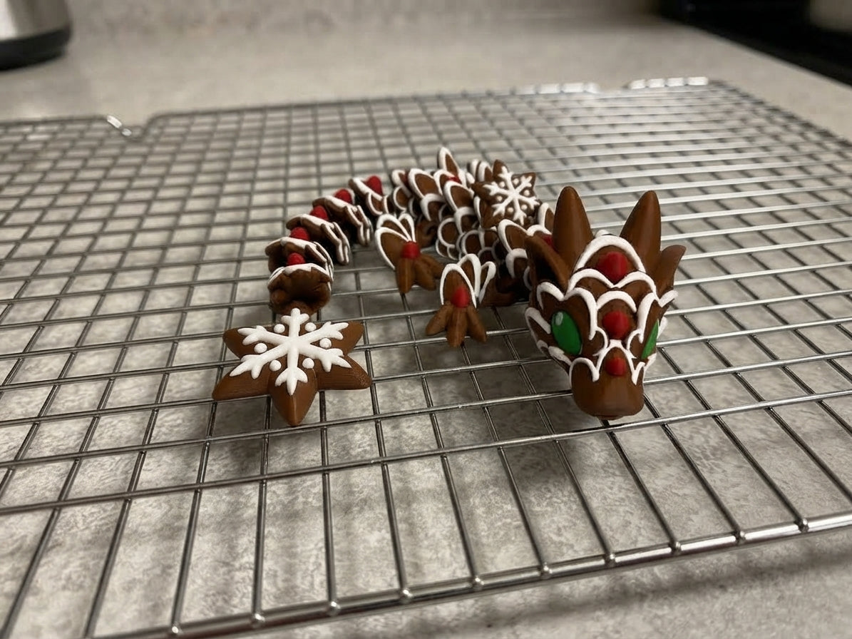 A decorated gingerbread dragon figurine with a snowflake cookie, displayed on a metal cooling rack over a gray countertop.